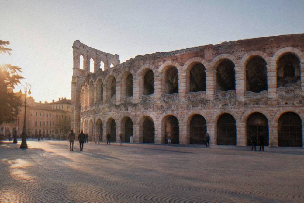 The arched outer wall of the Arena di Verona seen from the open paving of Piazza Bra under a clear sky