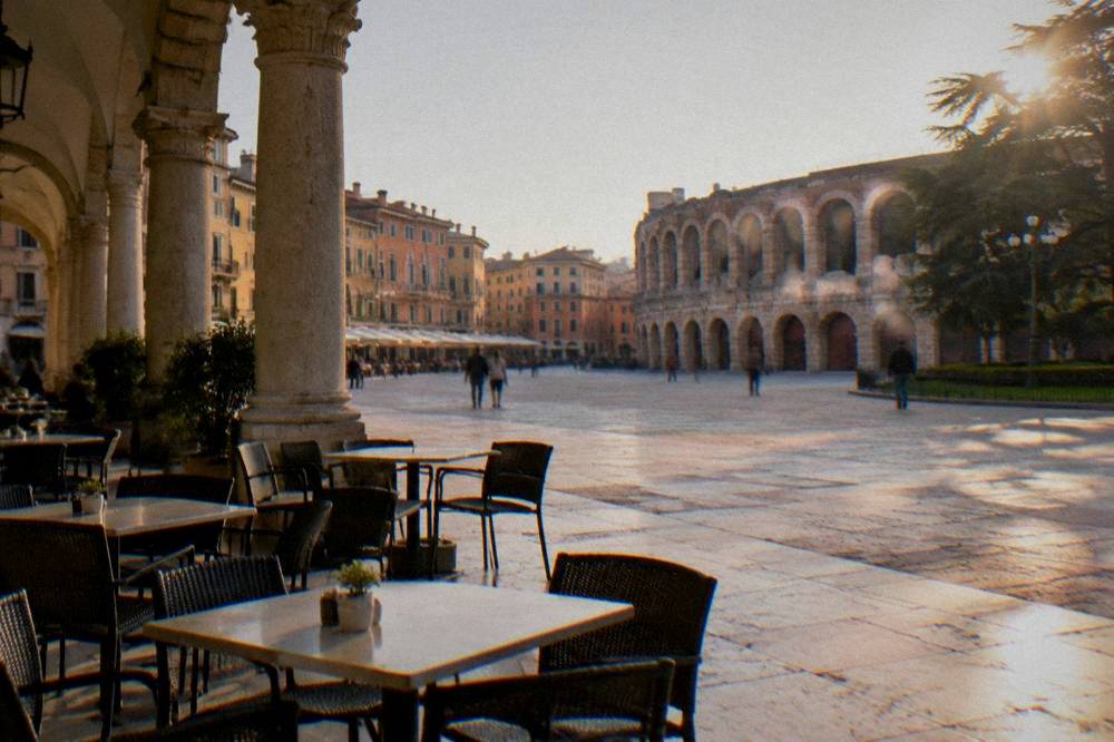 Cafe tables and chairs set out on marble paving beside a historic arcade near Piazza Bra in Verona