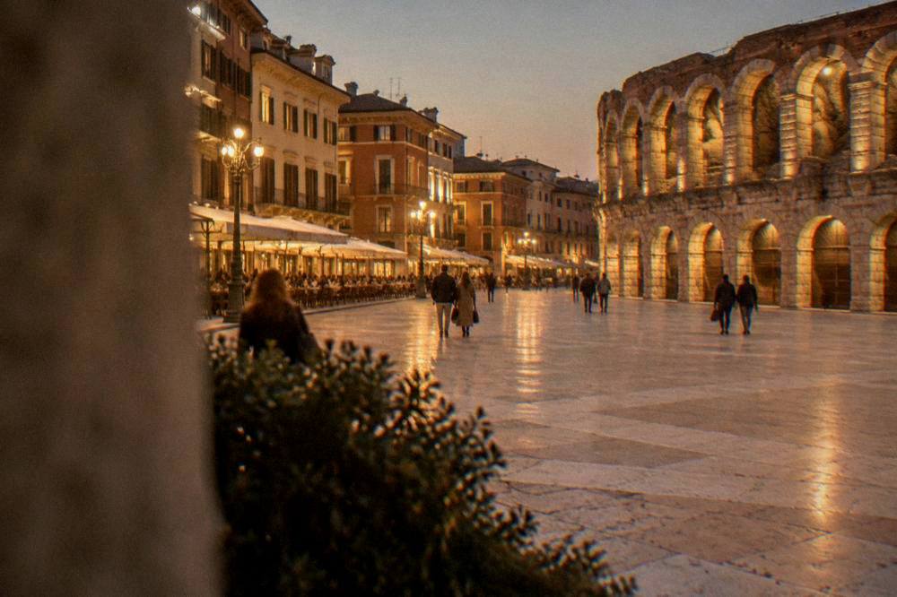 Night view of Piazza Bra with the Arena's illuminated arches and warm light from cafe terraces along the Liston