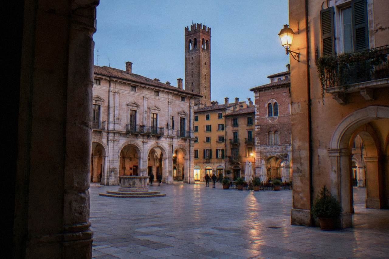 A quiet medieval square in Verona with a statue of Dante standing above stone paving and historic palace facades