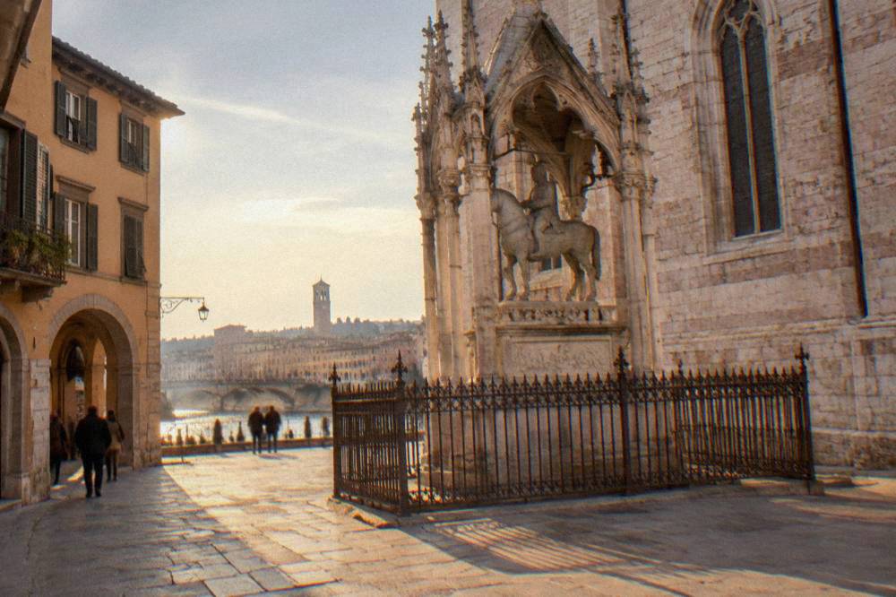 Gothic stone tomb with an equestrian statue inside wrought iron fencing beside a church in Verona