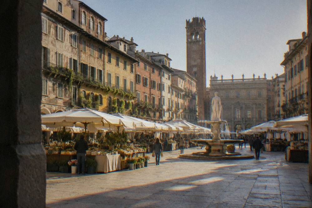 Fountain and market awnings in a sunlit square surrounded by old painted buildings