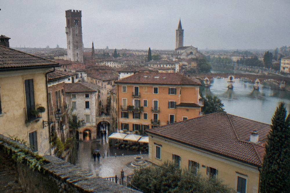 Tall medieval stone tower rising above red rooftops and a church tower in Verona