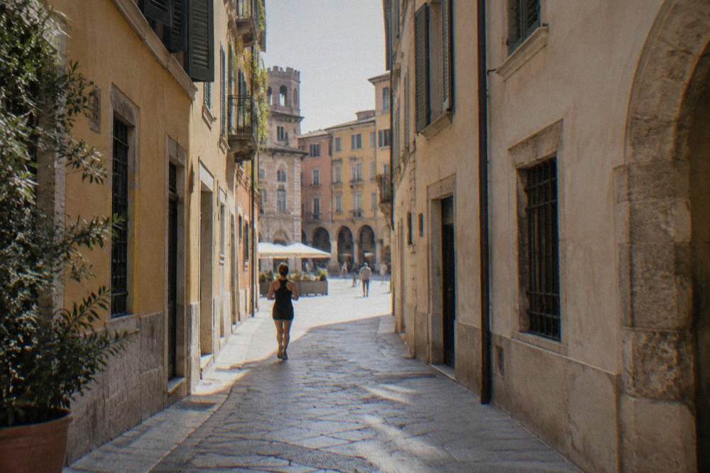Narrow pedestrian lane in Verona lined with old buildings leading toward a bright square