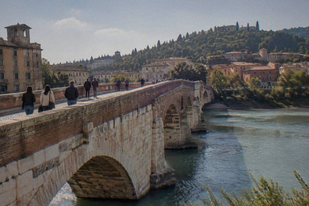 Pedestrians walking across an old stone bridge with the river flowing beneath the arches