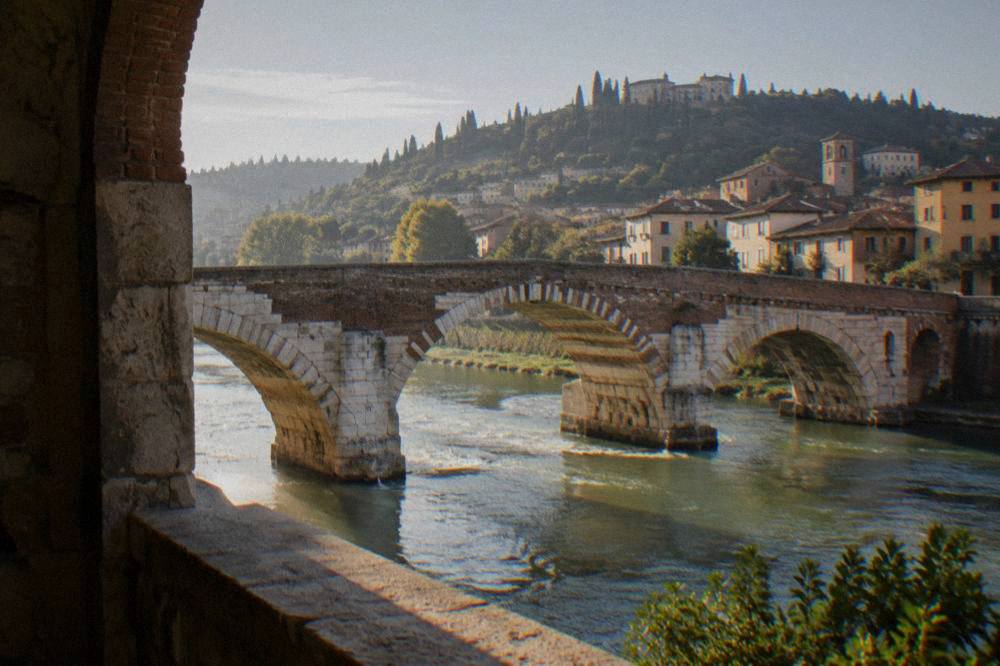 An old stone bridge over a river in soft morning light with hills behind