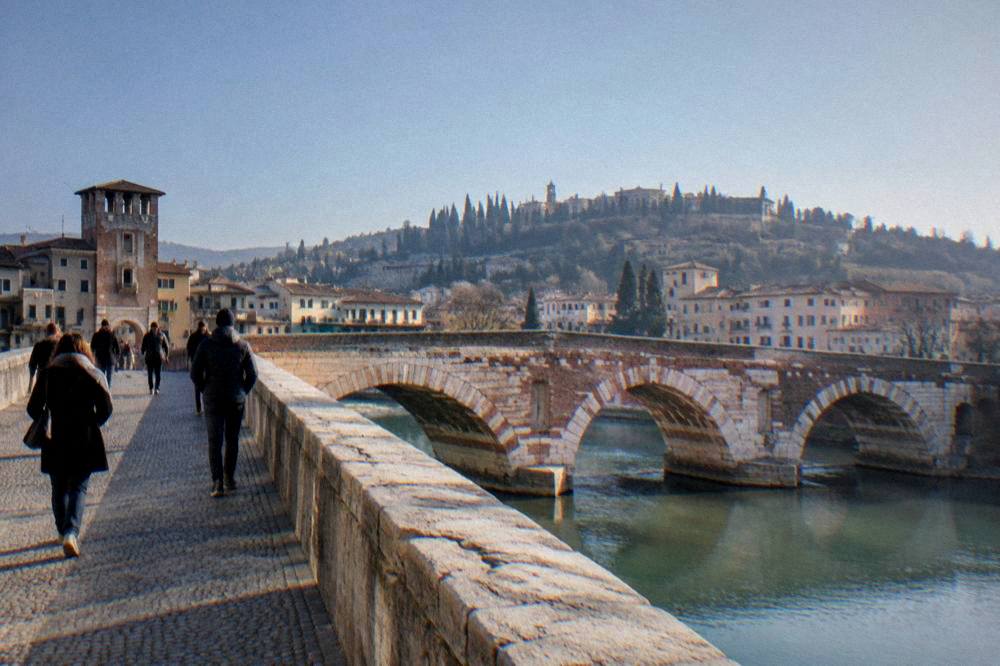 A level stone pedestrian bridge deck with worn cobblestones and people strolling