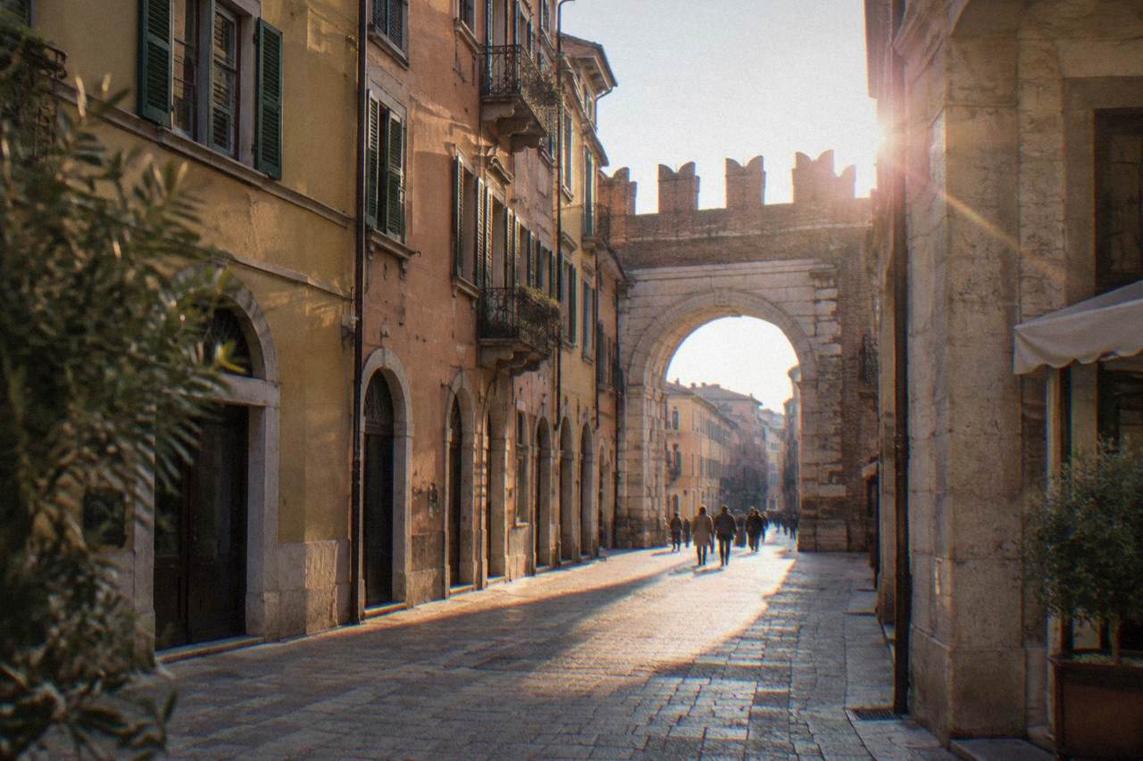 Roman stone gate with arched openings at the junction of a pedestrian street and a wide piazza