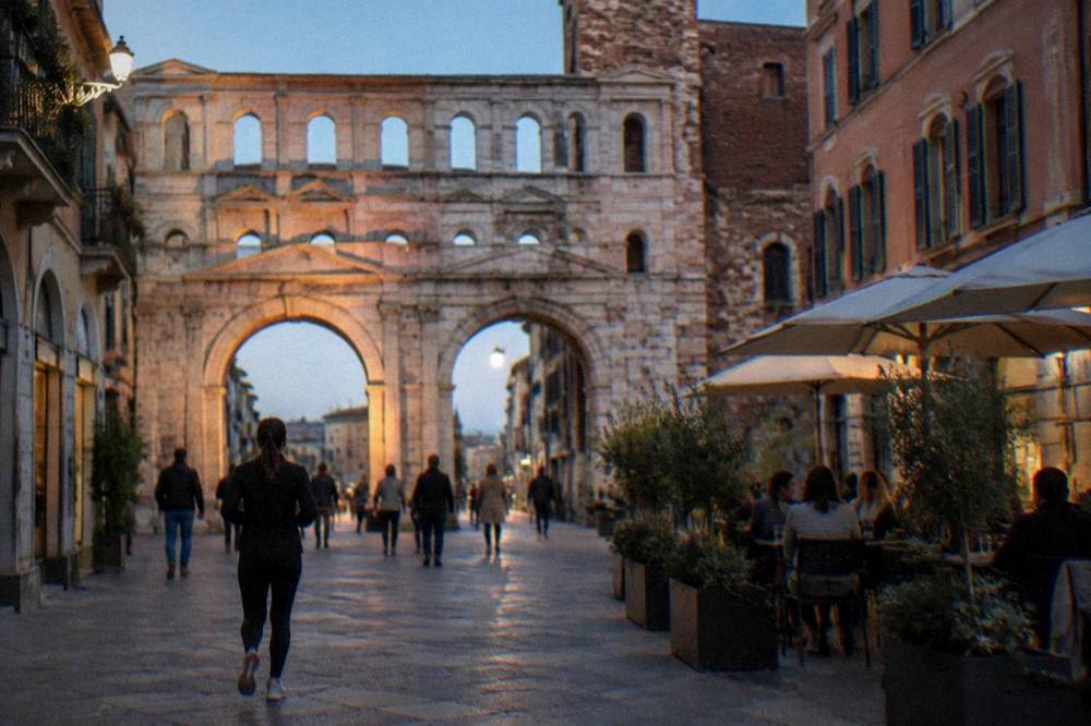 Ancient archway lit by low evening sun with people sitting at nearby cafe tables