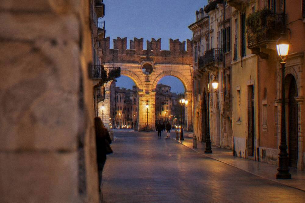 Evening view of an illuminated Roman gate at the end of a lamplit street in Verona