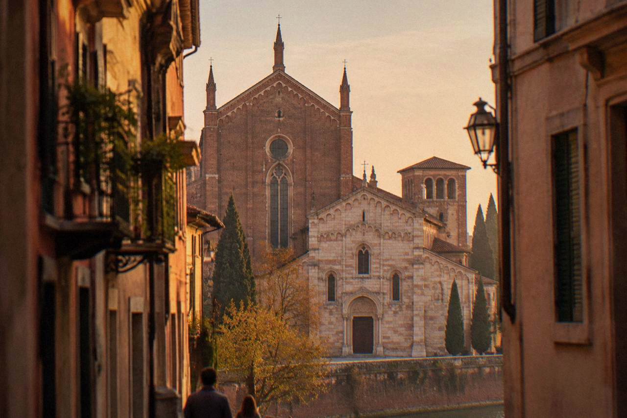 The brick and stone facade of the San Fermo Maggiore basilica in Verona seen from the street below