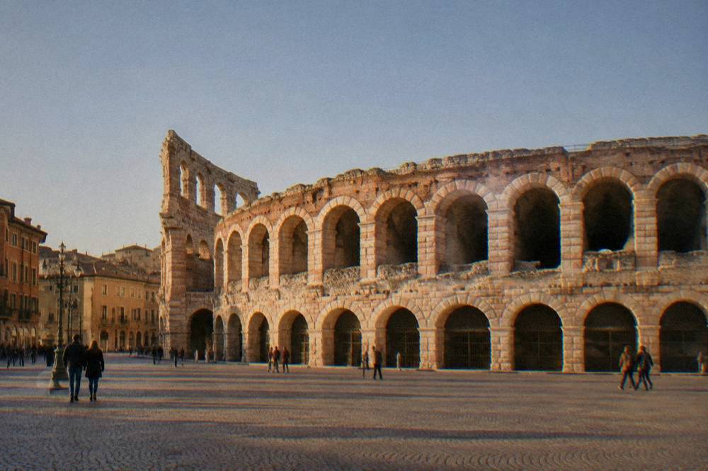 A small group of visitors listening to a guide in a sunlit Verona square near old palace walls