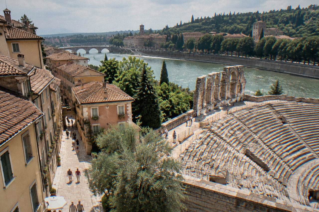 The stone tiers of the Roman theatre in Verona rising above the Adige river with trees on the far hillside