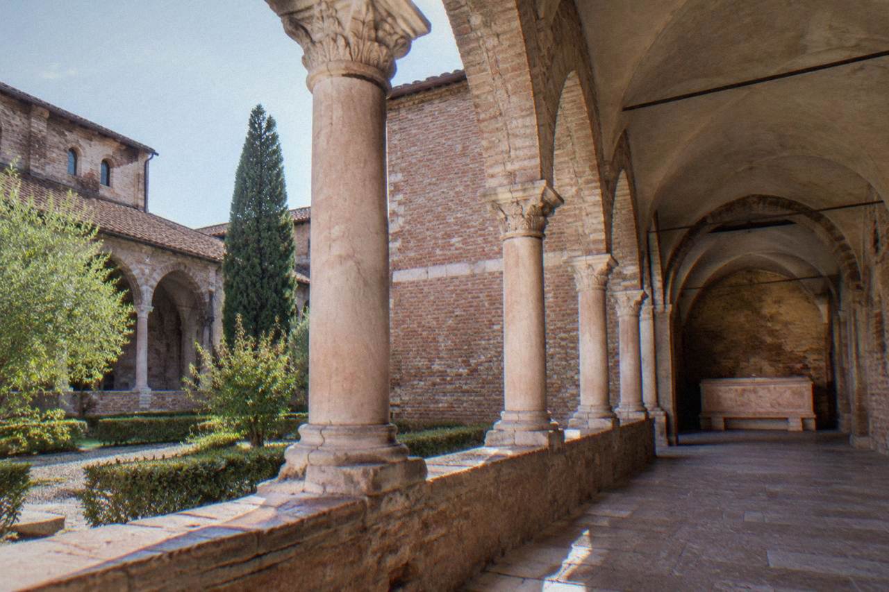 A quiet stone cloister walkway with arched columns and worn brick walls in soft afternoon light