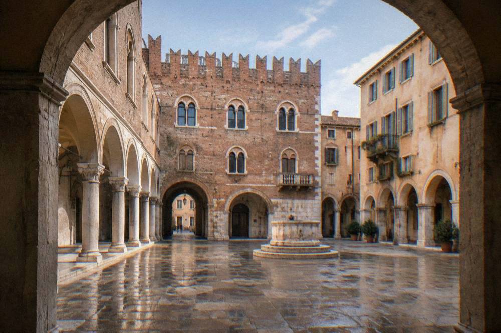 A medieval brick courtyard in Verona seen from under an archway, with empty stone arcades