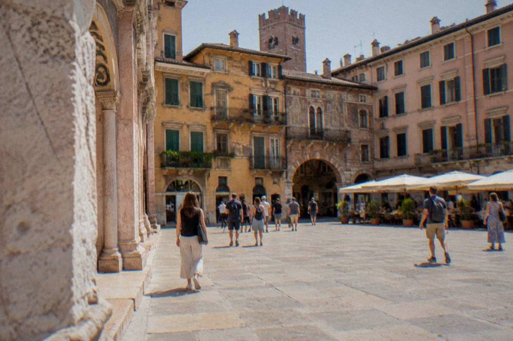 Tourists crossing a sunlit Verona square lined with historic painted buildings