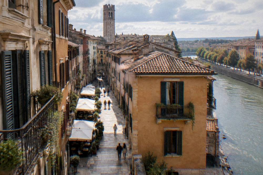 A pedestrian lane in central Verona with cafes and old facades leading toward a stone tower