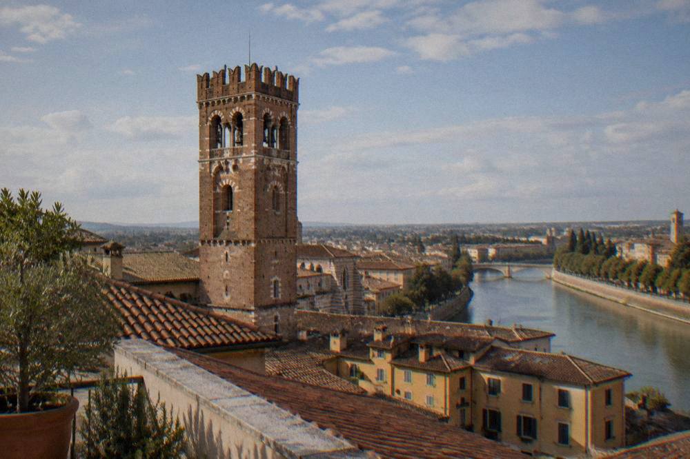 The upper belfry and arches of a medieval tower in Verona seen from a rooftop terrace below
