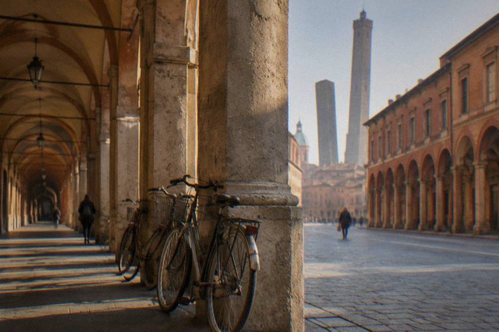 An arcade of stone arches along a Bologna sidewalk with bicycles leaning against a column