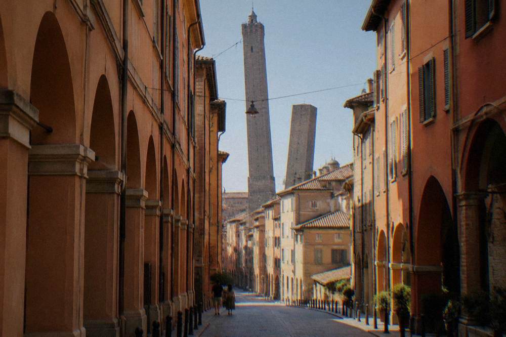 Two brick towers rising over rooftops at the end of a narrow Bologna street