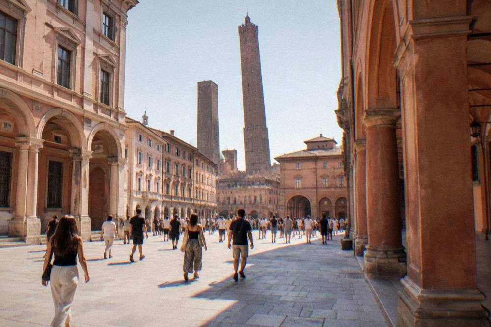 A wide Verona piazza with pink marble buildings and a crowd crossing toward an arched gateway