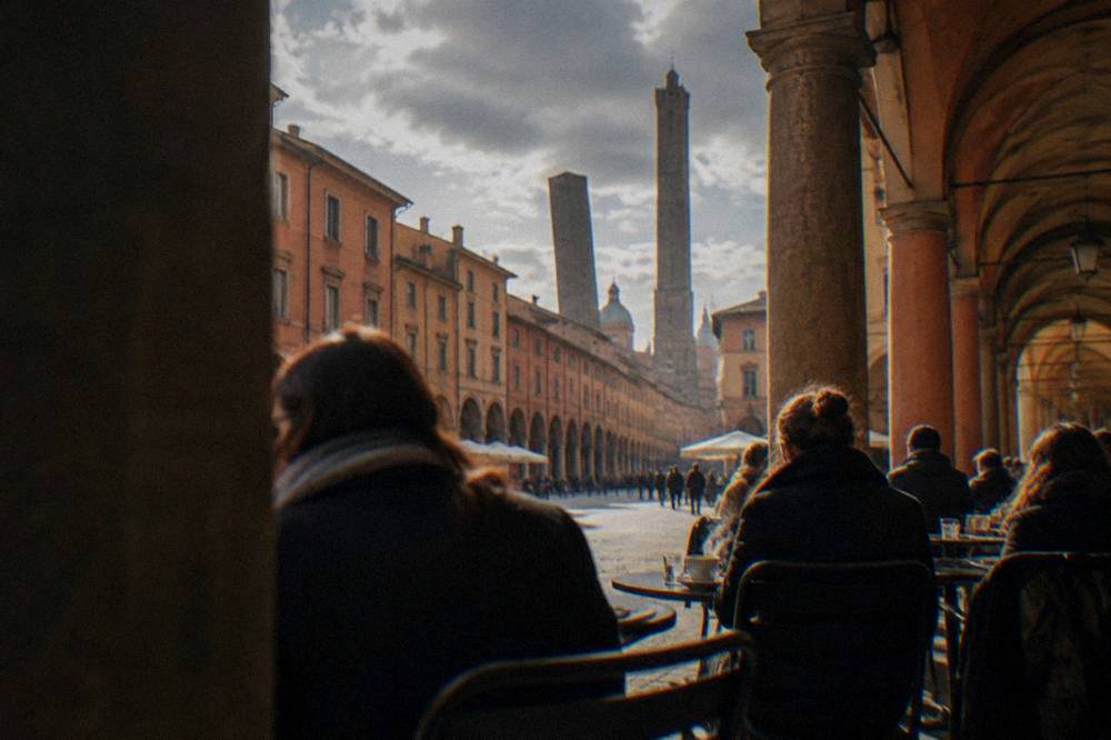 People sitting at outdoor tables under arcade arches with coats on and steam rising from cups