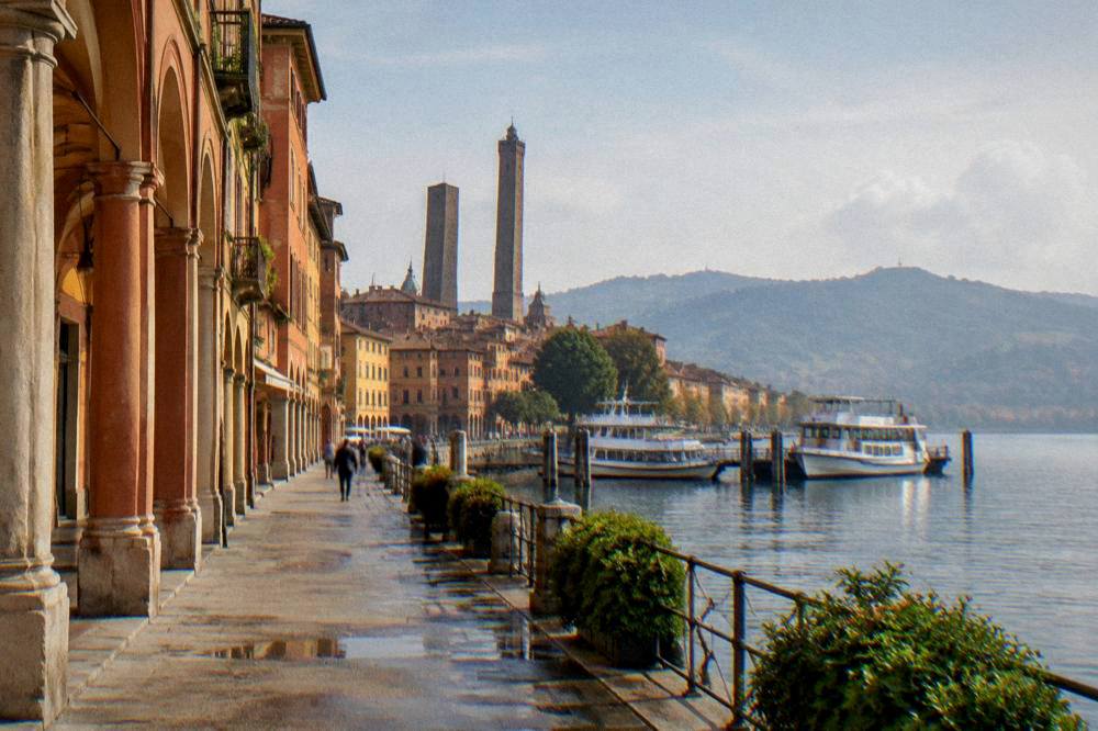 A lakeside promenade with ferry boats moored at a pier and hills rising across the water