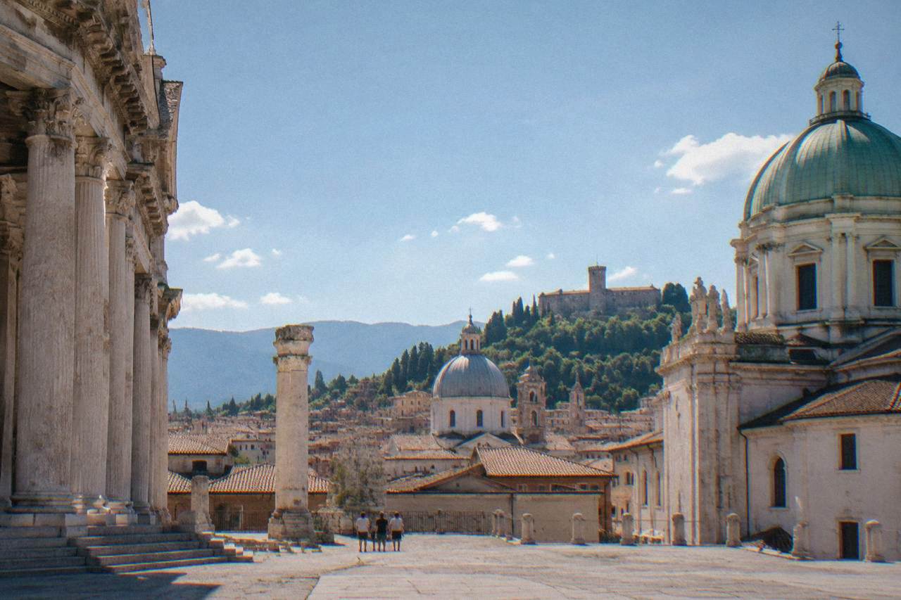A view over rooftops and church domes toward hills on the horizon in a northern Italian city