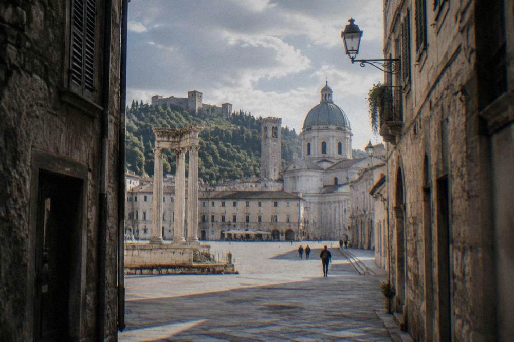 A narrow medieval Italian street with stone buildings and shuttered windows in morning light