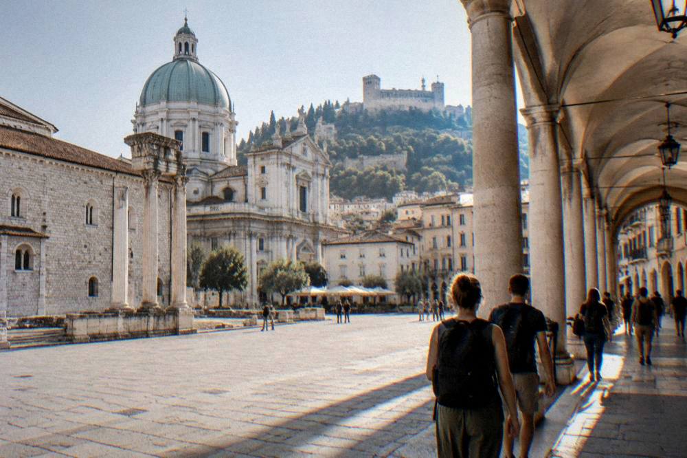 Travellers with backpacks walking through an arcaded Italian shopping street in late afternoon light