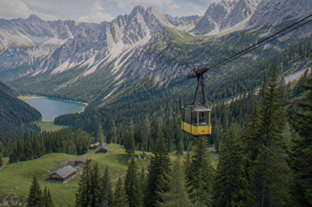 A yellow cable car cabin crossing a forested slope with a lake visible far below