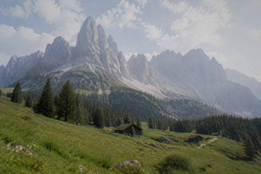 White limestone peaks with green alpine meadows in the foreground under scattered clouds