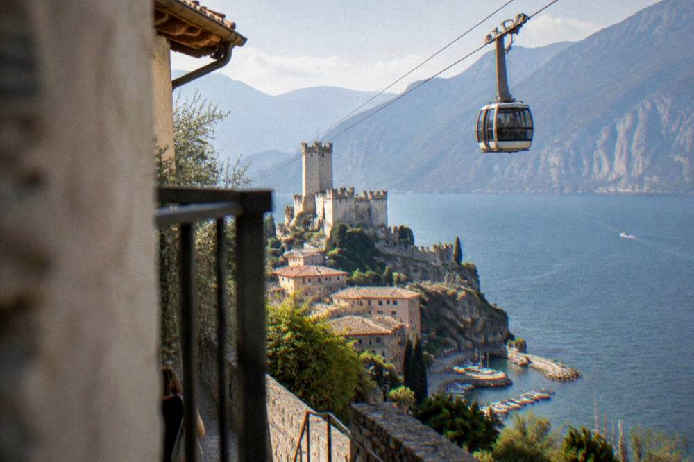 A cable car cabin rising above Malcesine with the blue lake and mountains spread below