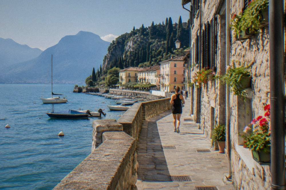 A narrow lakeside street with stone buildings, window boxes and a glimpse of water