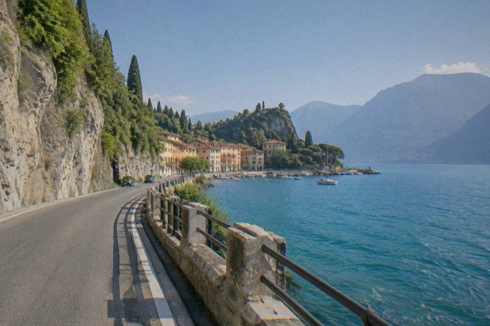 A winding lakeside road with rock cliffs above and blue water below on Lake Garda