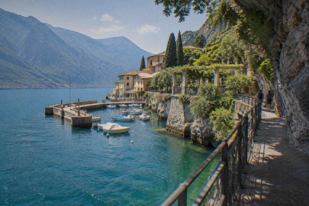 A narrow walkway anchored to a rock cliff with turquoise water below and mountains across the lake