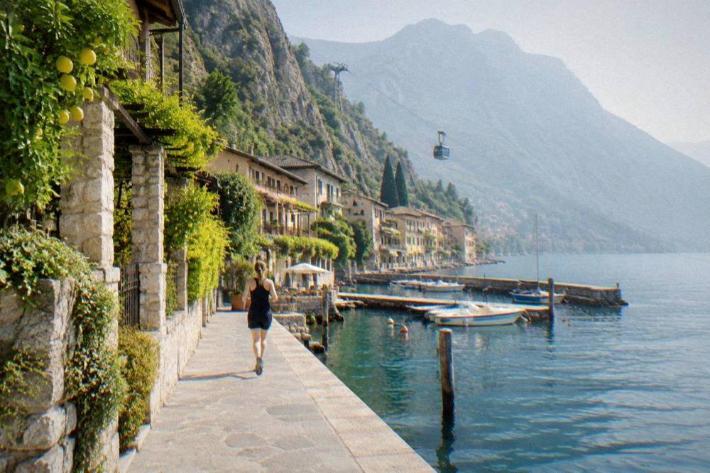 A cable car cabin rising above a lakeside town towards a bare mountain ridge