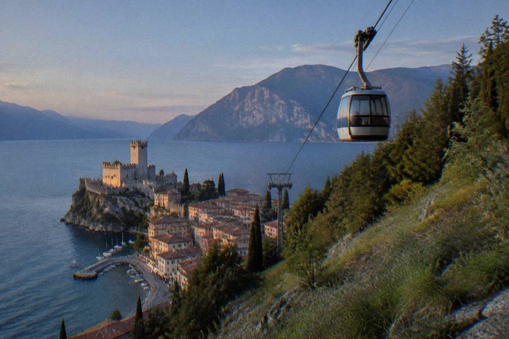 A cable car cabin ascending above forested slopes toward an open mountain ridge
