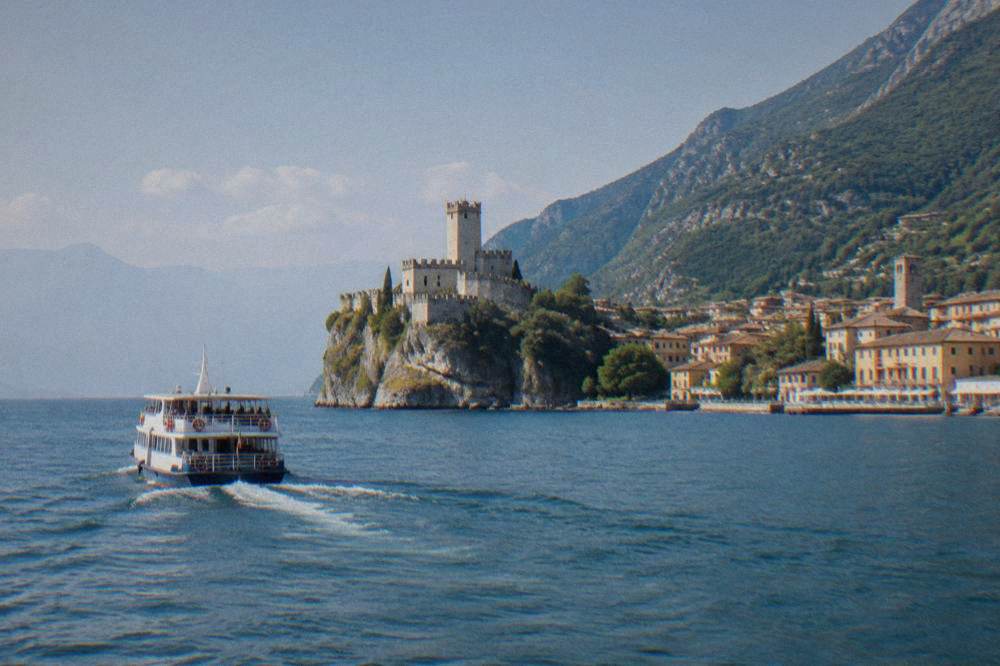 Wooden dining tables beside a stone harbour wall with small boats and castle tower beyond