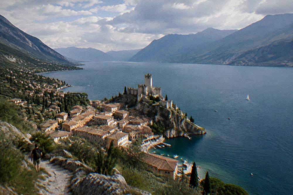 Evening light over a lake harbour with castle walls and mountains fading into haze