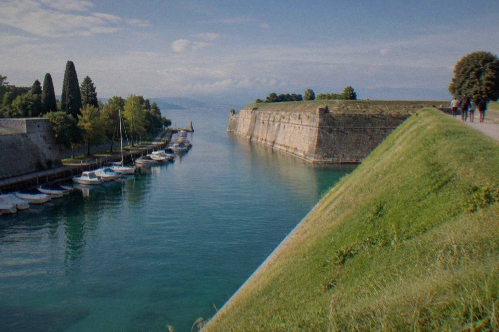 Walkers on the grassy ramparts of the Peschiera del Garda fortress walls with the lake beyond