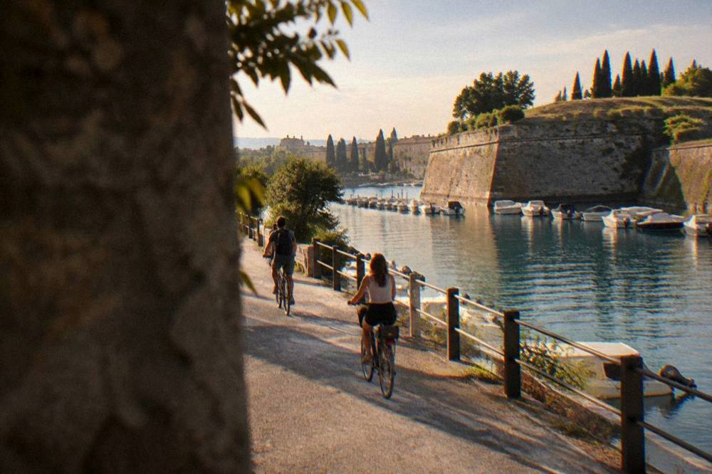Cyclists on a flat lakeside path near Peschiera del Garda with the water on one side