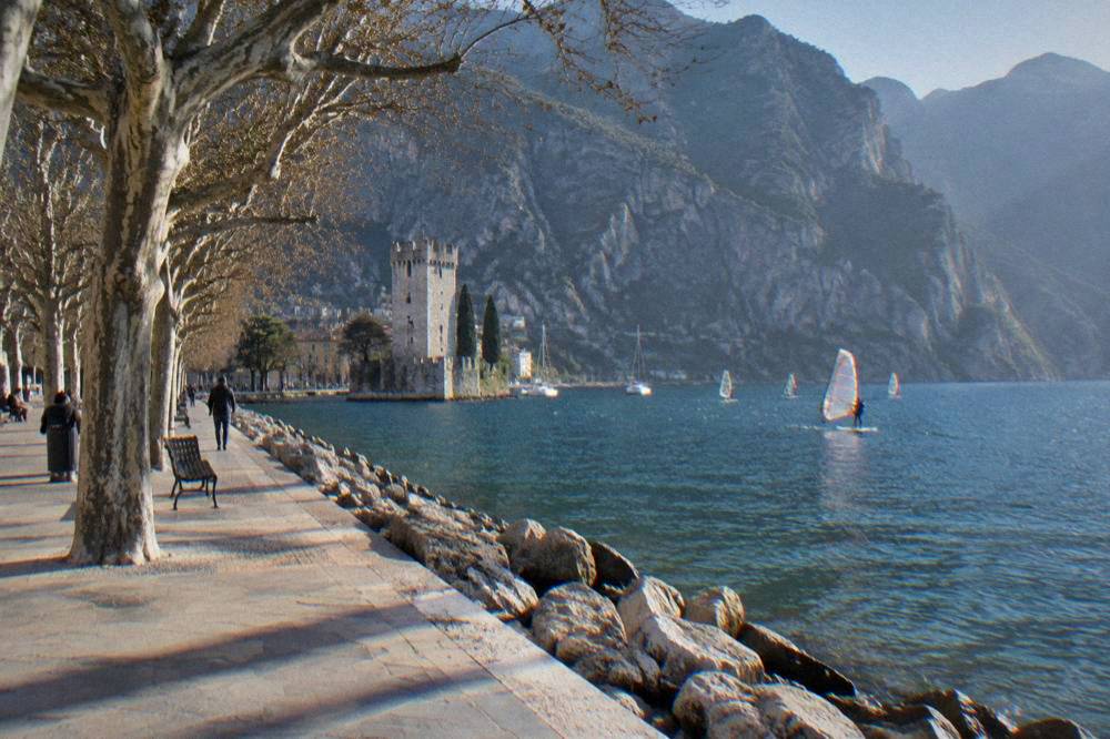 Windsurf sails out on the water near Riva del Garda with cliffs rising behind the shore