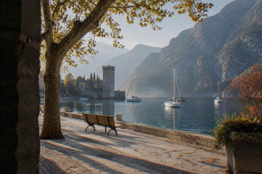A quiet lakefront in early autumn with empty benches and still water below the mountains