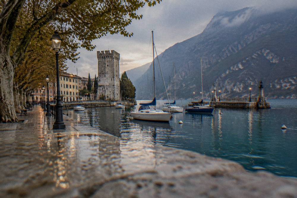 The historic harbour mole of Riva del Garda with lanterns and moored boats in evening light