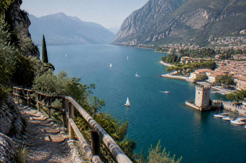 A view from a cliff path above the lake showing the long northern shoreline curving towards Riva del Garda