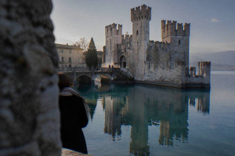 The crenellated wall of a lakeside castle reflected in still water at dusk