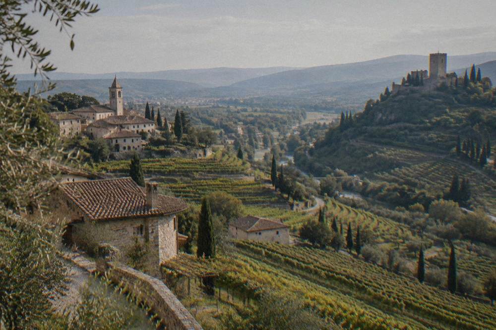A stone castle keep on a hilltop overlooking vineyards and a valley