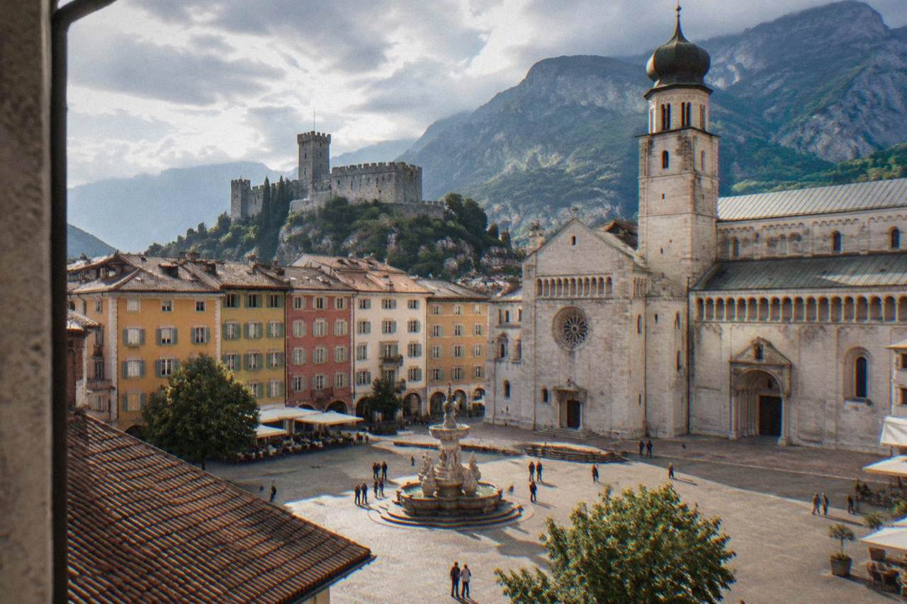 A north Italian alpine town with pastel painted facades and mountains rising behind the rooftops