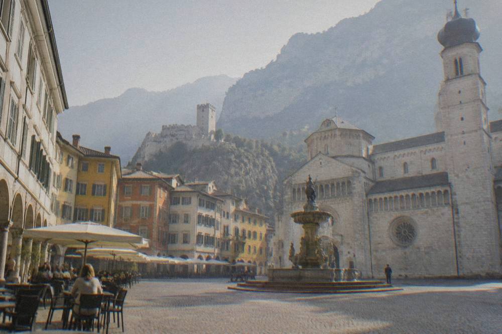 A quiet square with outdoor cafe tables under arcades in the late afternoon